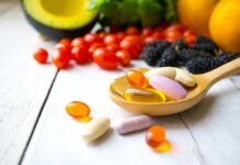 Common Vitamin Delivers Surprising Cancer Punch Wooden spoon holding assorted vitamin pills beside fresh fruits and vegetables