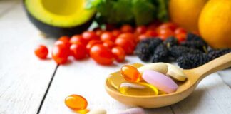 Wooden spoon holding assorted vitamin pills beside fresh fruits and vegetables