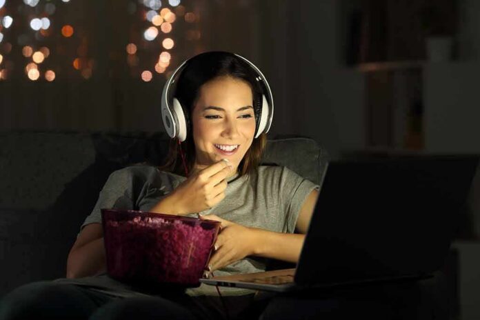 Woman wearing headphones watching a laptop with a bowl of popcorn