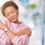 Woman in pink sweater hugging herself with eyes closed