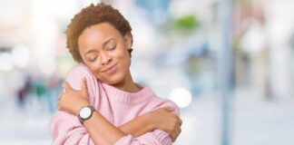 Woman in pink sweater hugging herself with eyes closed