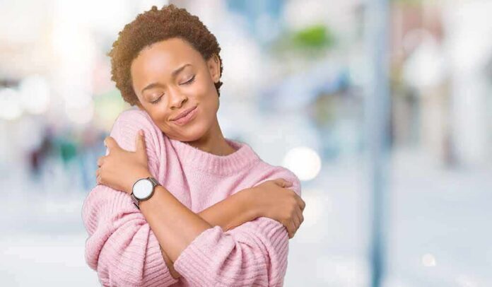 Woman in pink sweater hugging herself with eyes closed