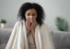 Why You Keep Catching Colds (5 Remedies That Actually Help) Woman wrapped in a blanket blowing her nose