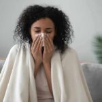 Woman wrapped in a blanket blowing her nose