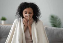 Why You Keep Catching Colds (5 Remedies That Actually Help) Woman wrapped in a blanket blowing her nose