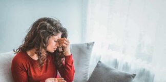Woman sitting on couch holding pills and rubbing her forehead