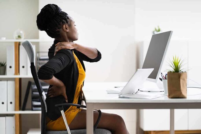 shutterstock_1787773679 Woman at desk rubbing her neck and lower back