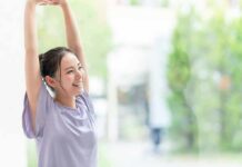 3 Tips To Slow Down Your Skin’s Biological Clock woman stretching with arms raised indoors near window