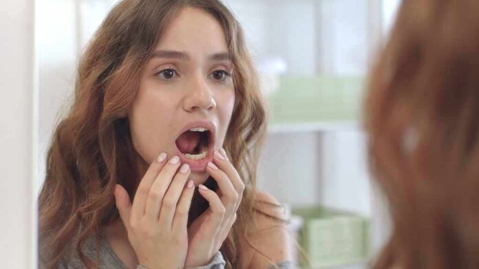 shutterstock_1817315312 young woman checking inside her mouth in bathroom mirror
