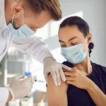 Healthcare worker giving a masked patient a vaccine in the upper arm