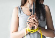 Woman with measuring tape around wrists holding fork and knife