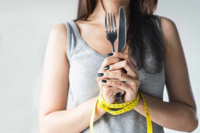 shutterstock_1926913811 Woman with measuring tape around wrists holding fork and knife
