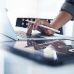 Person using laptop with stylus near tablet