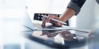 Person using laptop with stylus near tablet