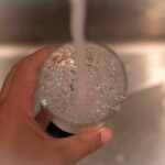 Hand holding a glass under a running faucet