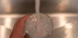 Hand holding a glass under a running faucet