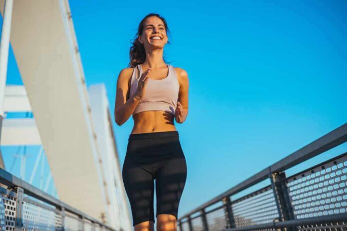 shutterstock_2623127963 Smiling woman jogging on a bridge under a clear blue sky