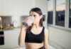 Gym Staple Tied To Tumor Fight Woman in sportswear drinking a smoothie in a kitchen