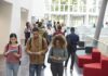 Students walking through a bright campus lobby using mobile devices