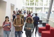 Students walking through a bright campus lobby using mobile devices