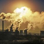 Industrial plant with smokestacks emitting thick smoke at sunset