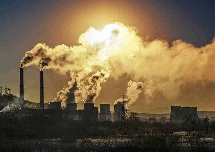 shutterstock_534462514 Industrial plant with smokestacks emitting thick smoke at sunset