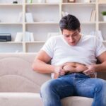 Manny MUA sitting on a couch pinching his belly