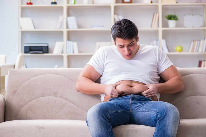 Manny MUA sitting on a couch pinching his belly