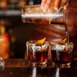 Bartender pouring cocktails into two rocks glasses